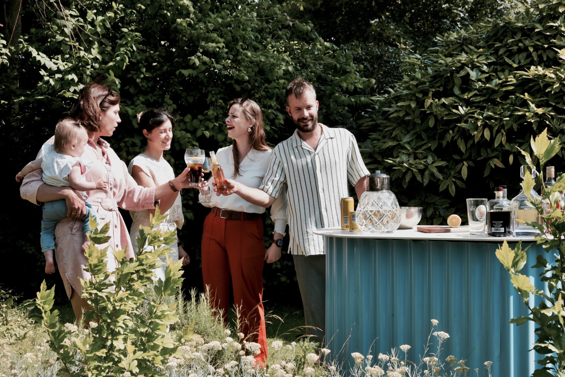 Vrienden klinken samen aan de blauwe KUJP Bar in de tuin